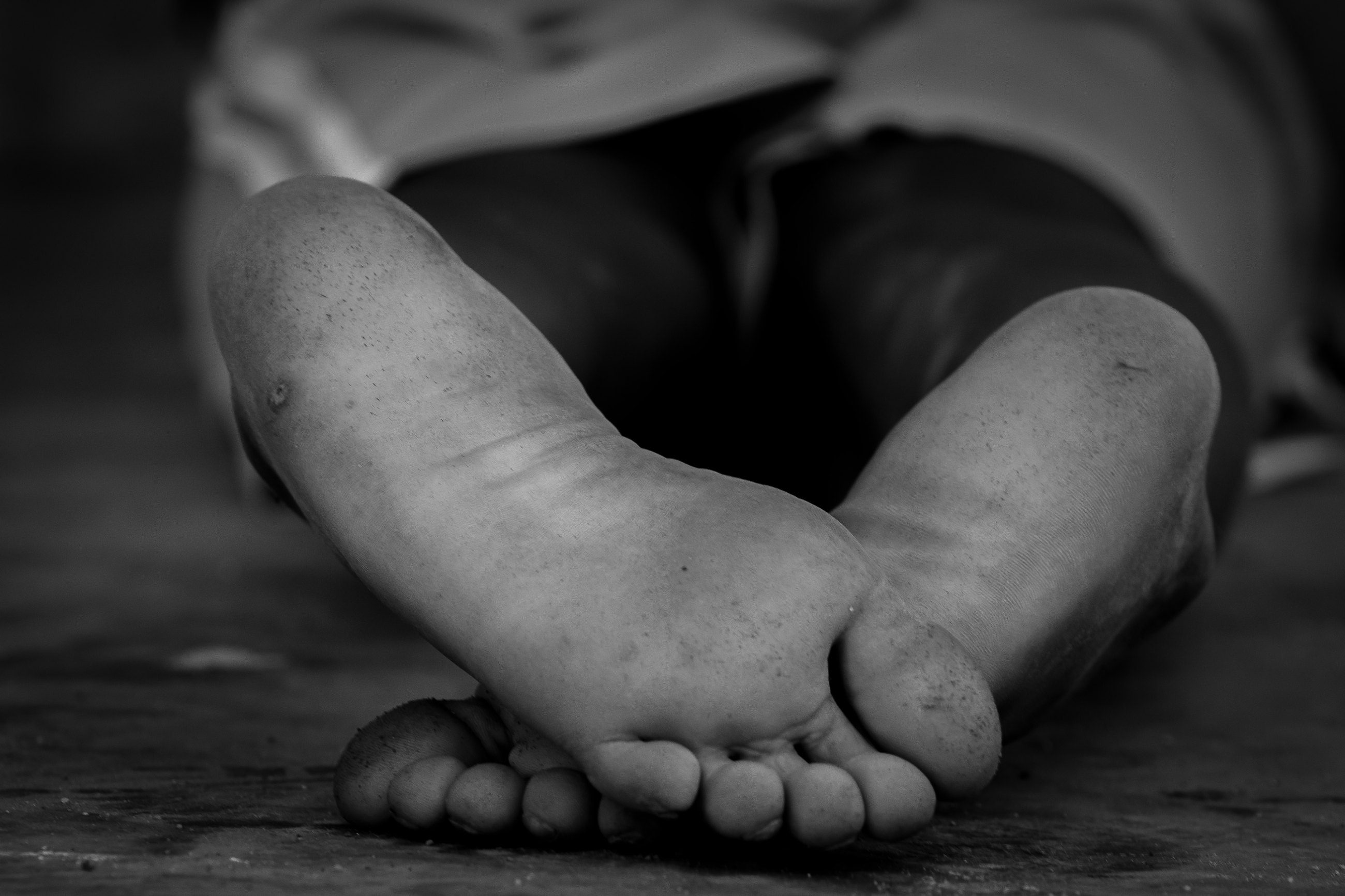 Close-up of the dusty bare soles of a child’s feet resting on a floor, in black and white