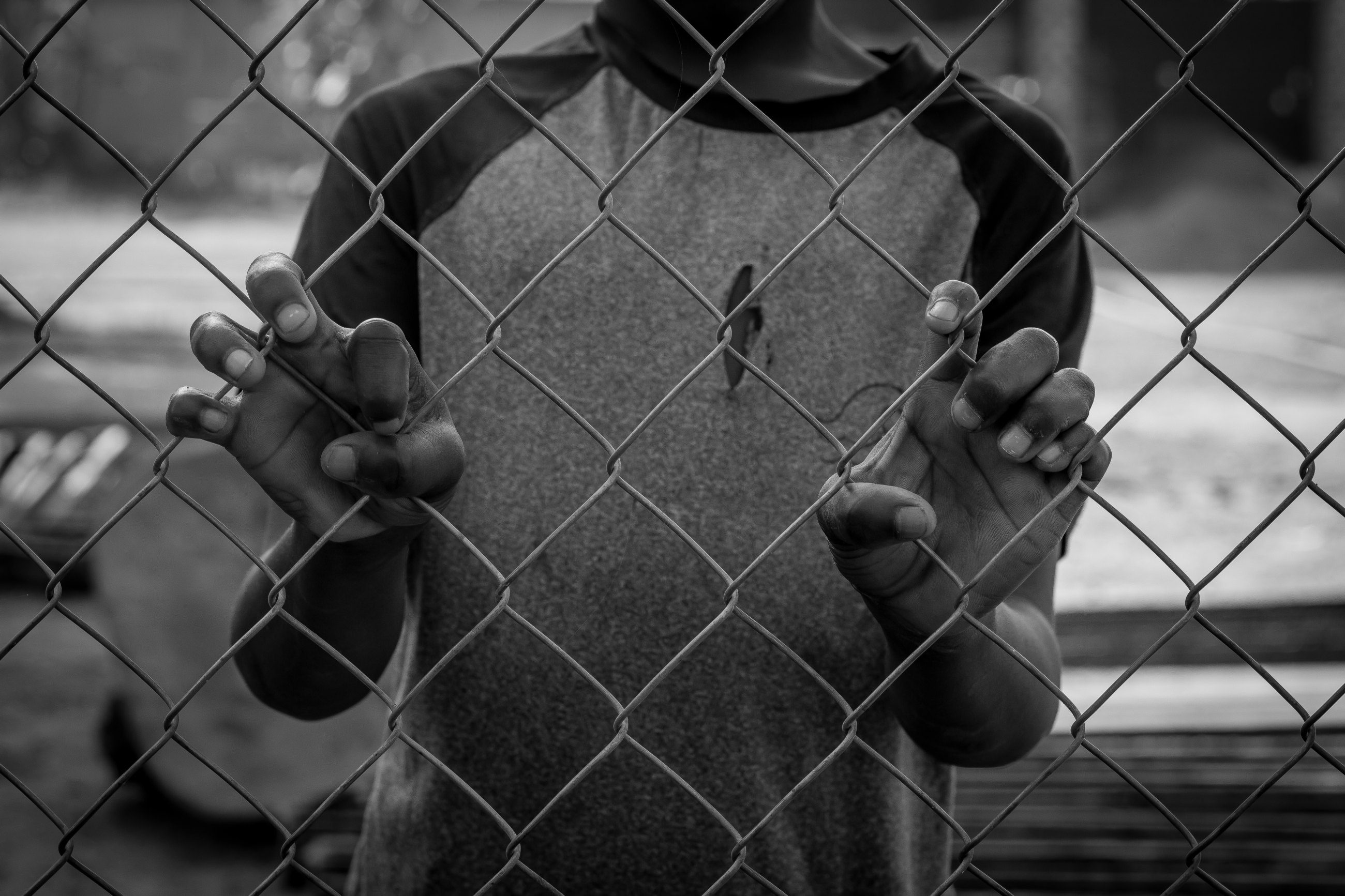 A child’s hands gripping a chain-link fence, in black and white
