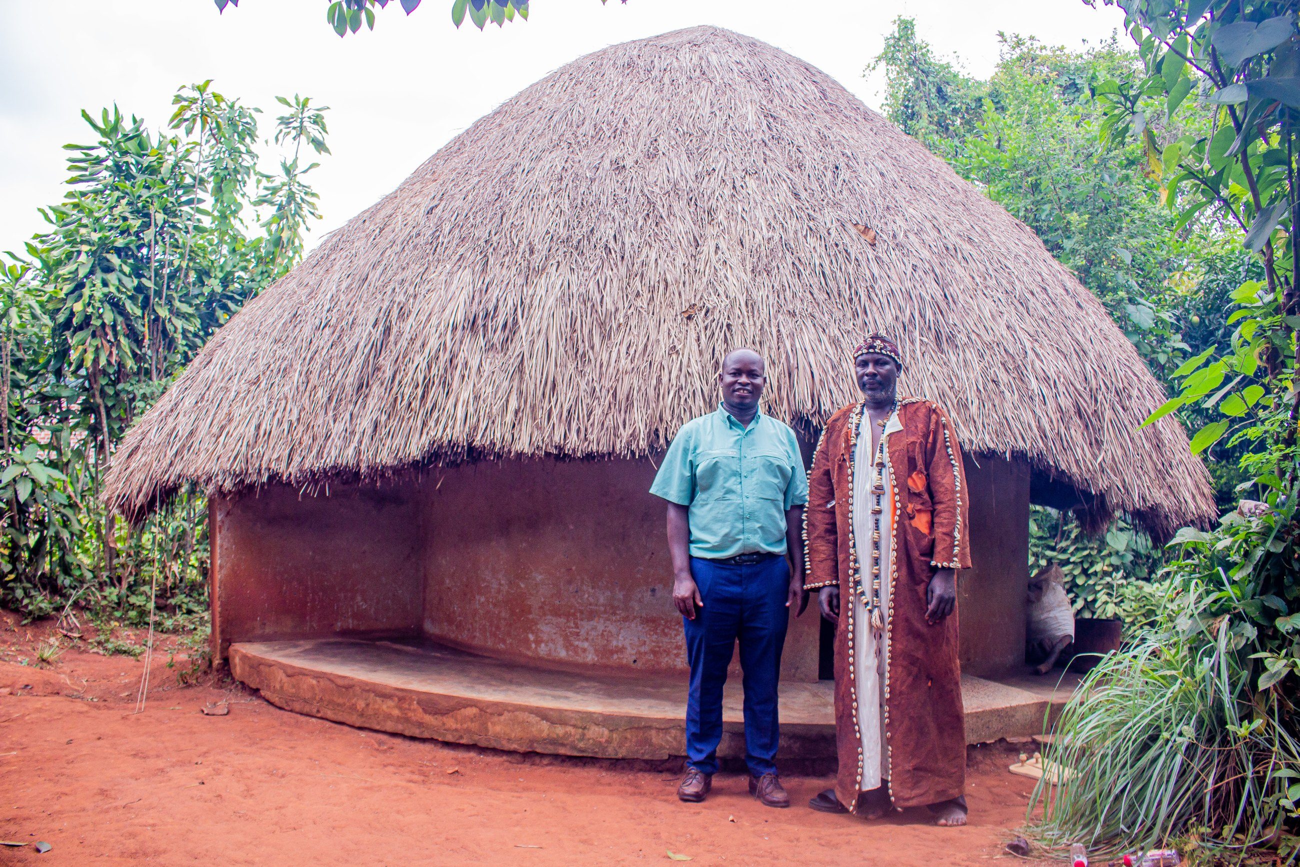 A Streams of Joy Services staff member and a traditional leader standing together in front of a thatched shrine