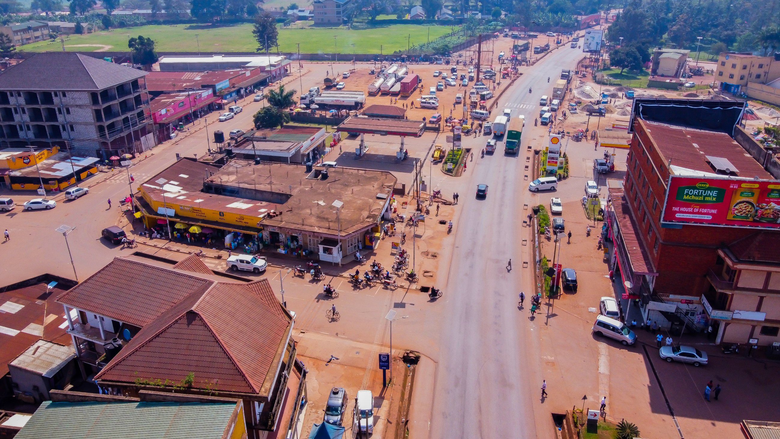 An aerial view of a busy town centre in Uganda, with a main road running between red-roofed shops and buildings