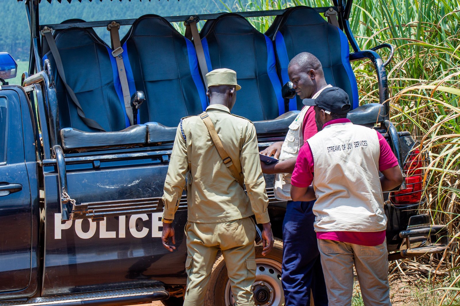 Streams of Joy Services staff and a Uganda Police officer conferring beside a police pickup on a rural road
