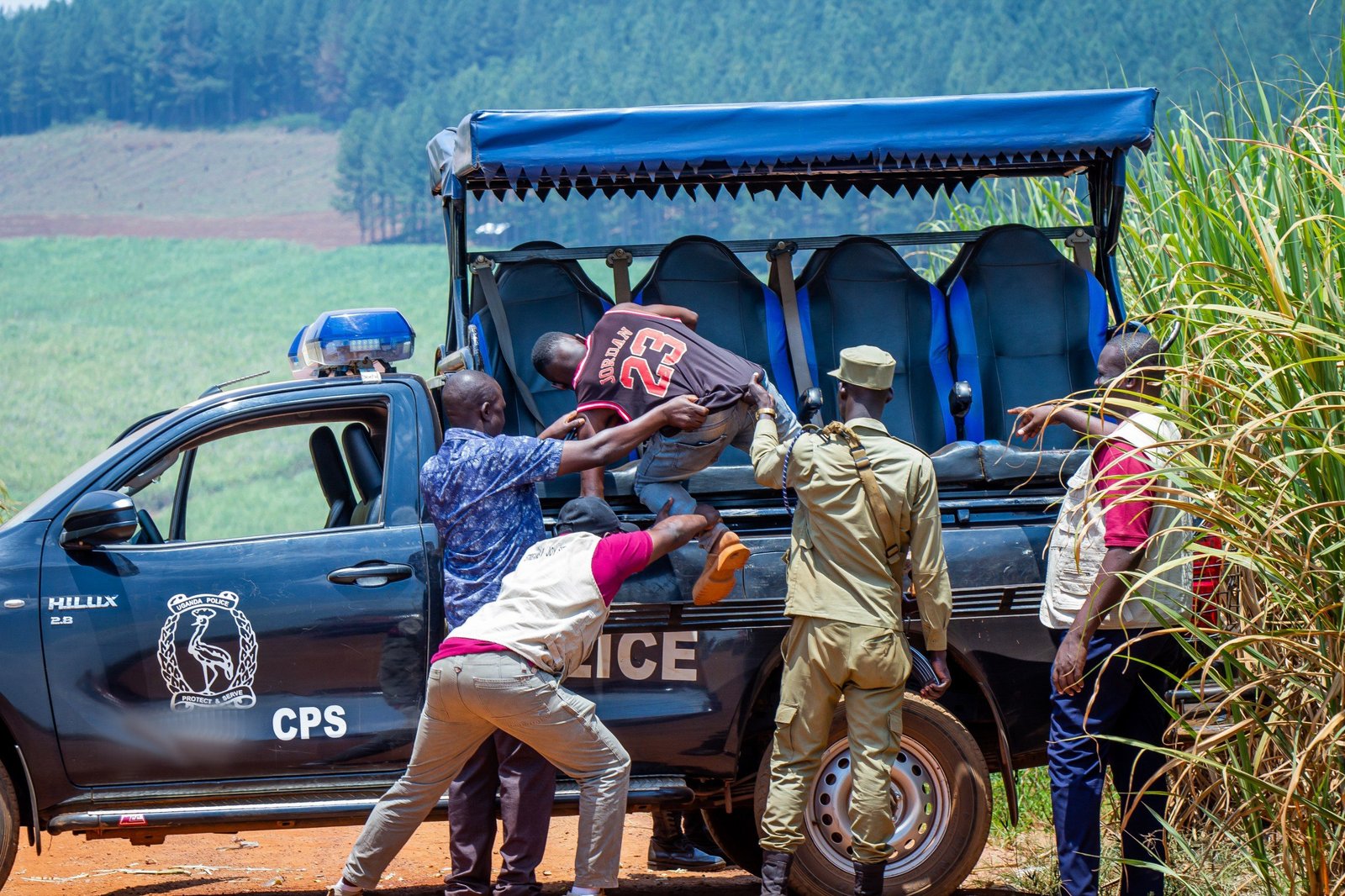 Streams of Joy staff and Uganda Police officers helping a rescued young person into a police pickup on a rural road