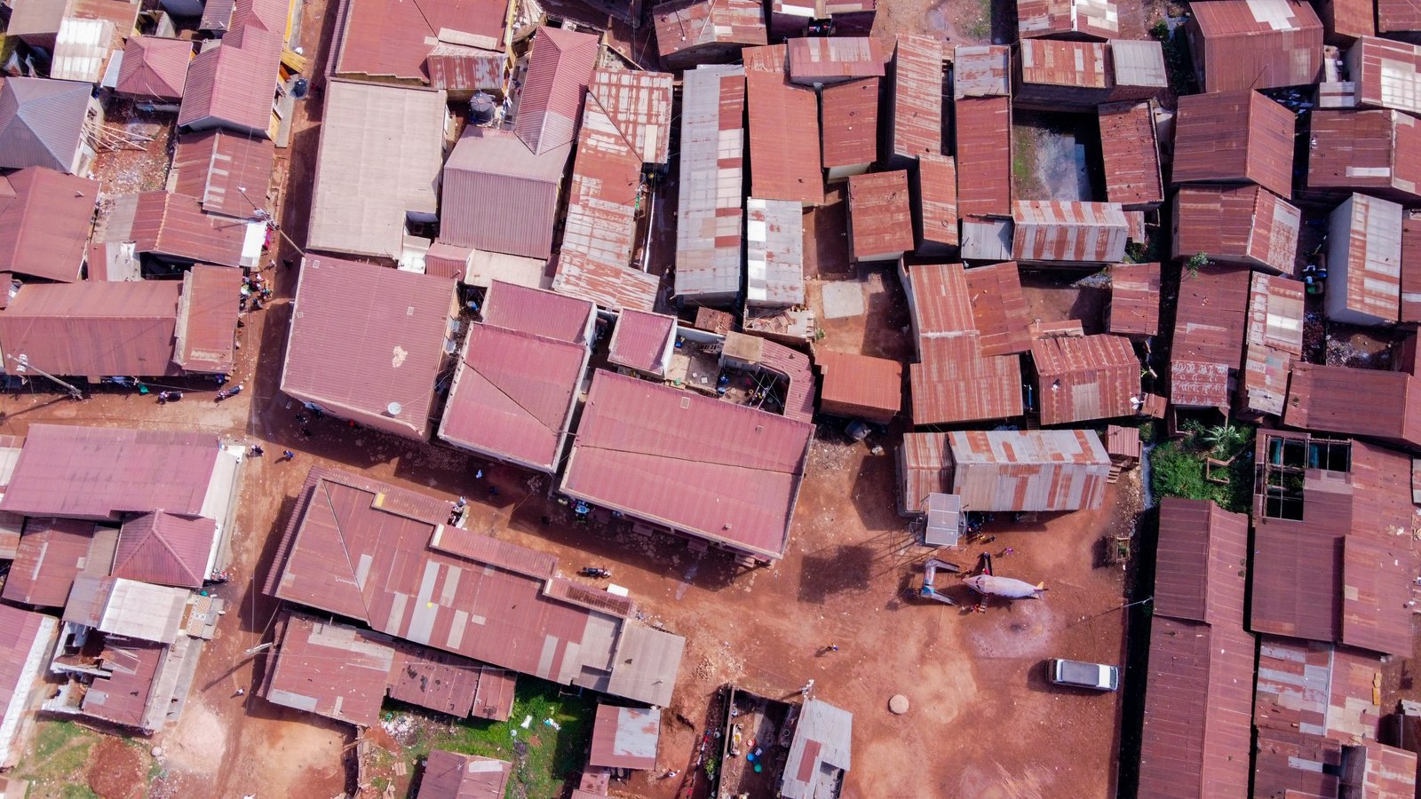 An aerial view of a densely built settlement of iron-roofed homes separated by narrow red earth paths