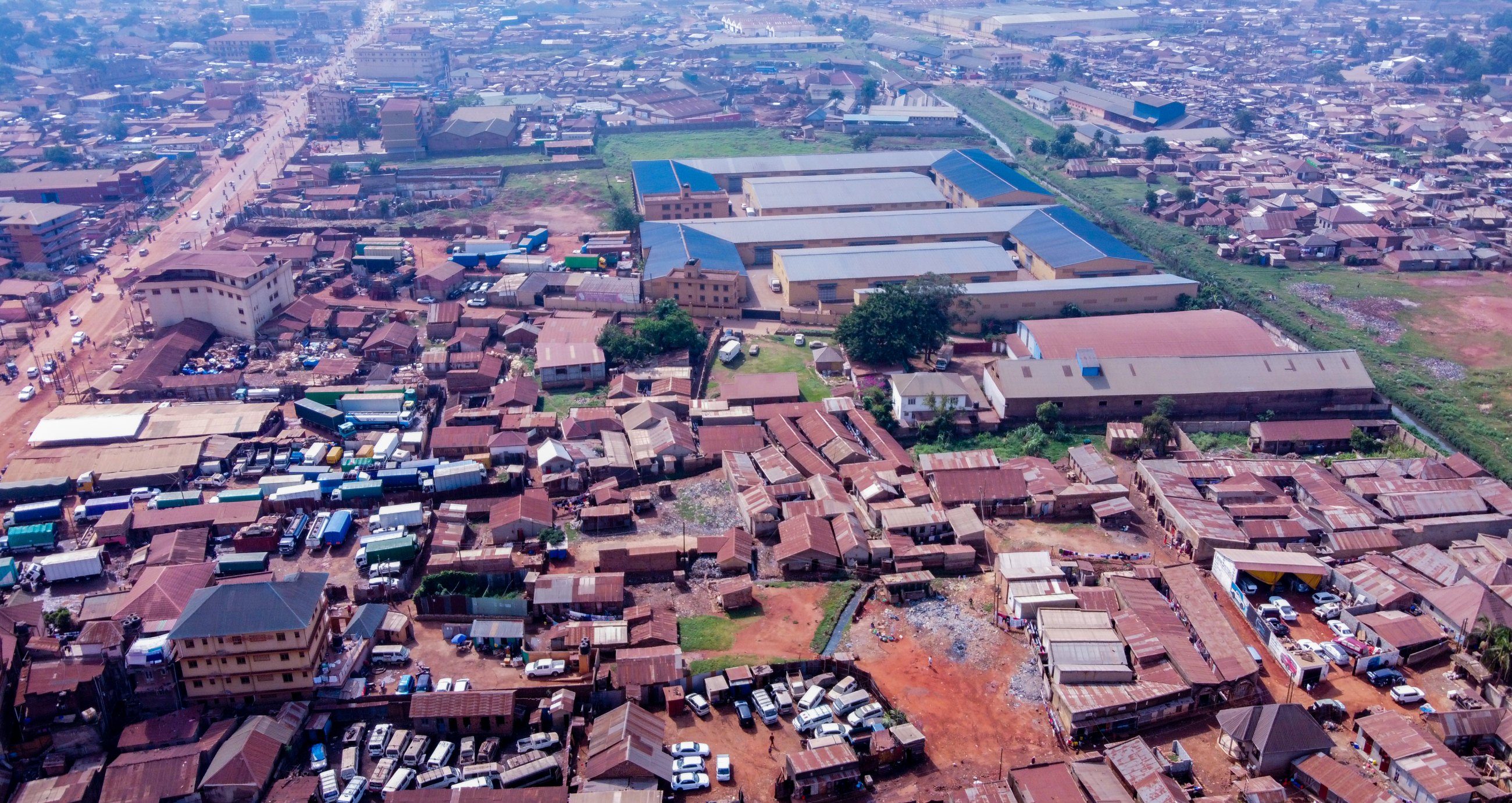 An aerial view over a Ugandan town, with a main road and markets running between red-roofed buildings